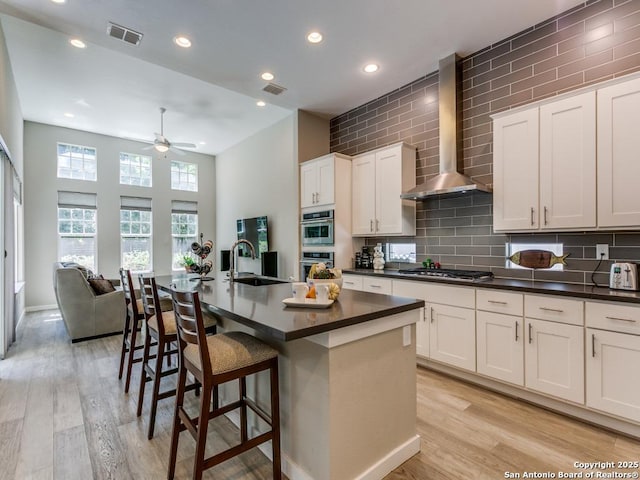 kitchen featuring sink, an island with sink, white cabinetry, and wall chimney exhaust hood