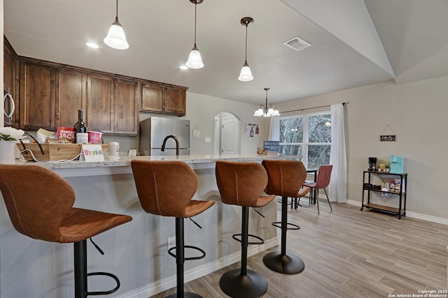 652 Canyon Bnd, Canyon Lake, TX 78133 - kitchen featuring a kitchen breakfast bar, light hardwood / wood-style flooring, decorative light fixtures, light stone countertops, and stainless steel refrigerator