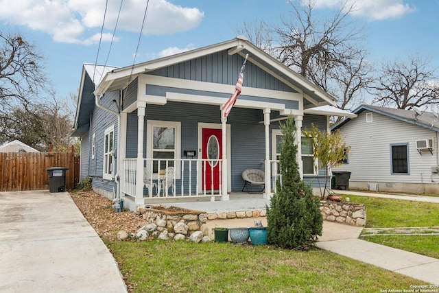 bungalow with a porch, a front yard, and a wall unit AC