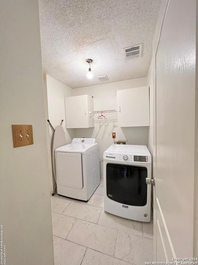 clothes washing area with cabinets, a textured ceiling, and washing machine and dryer