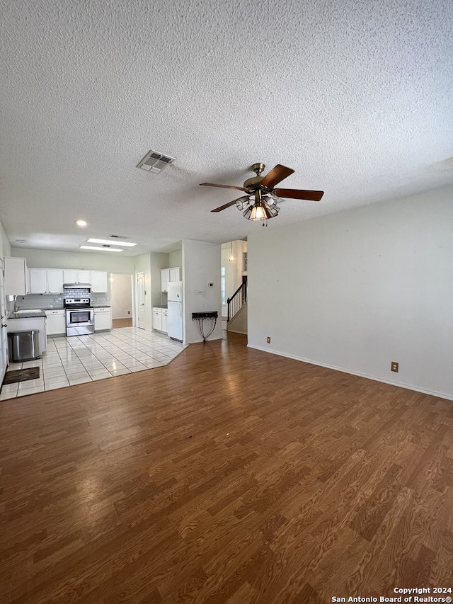 unfurnished living room featuring sink, light hardwood / wood-style floors, a textured ceiling, and ceiling fan