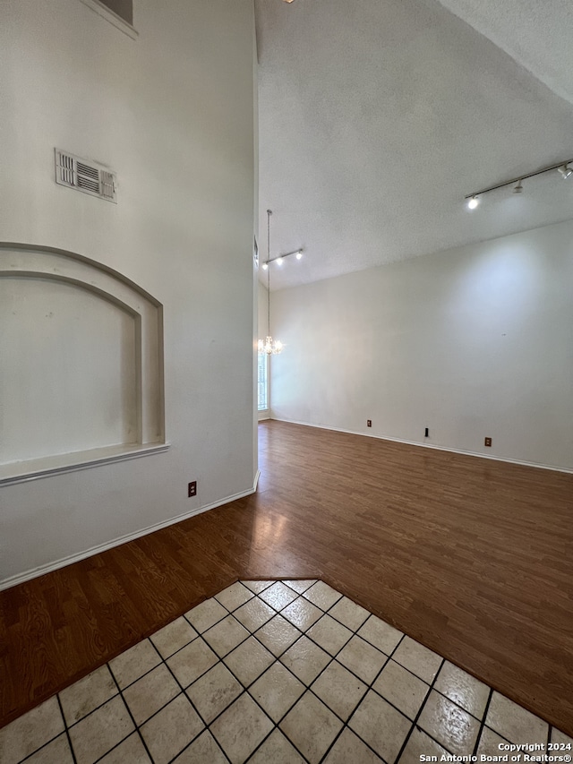 spare room featuring hardwood / wood-style floors, a textured ceiling, a towering ceiling, and a notable chandelier