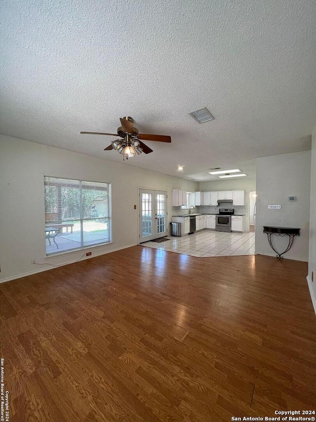 unfurnished living room with a textured ceiling, light hardwood / wood-style flooring, ceiling fan, and french doors