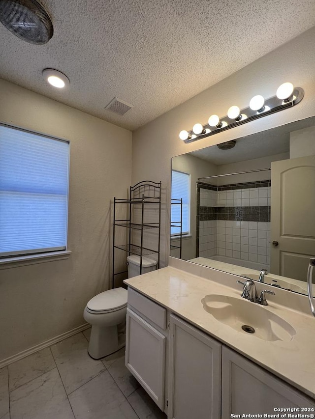 bathroom featuring vanity, toilet, tiled shower, and a textured ceiling