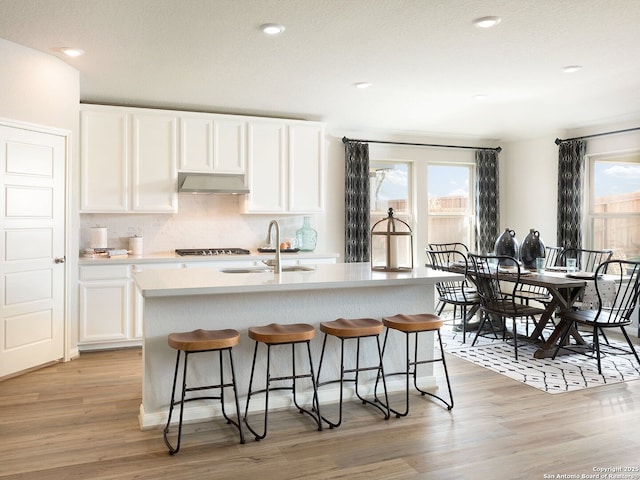 kitchen with white cabinets, light hardwood / wood-style floors, sink, a center island with sink, and range hood