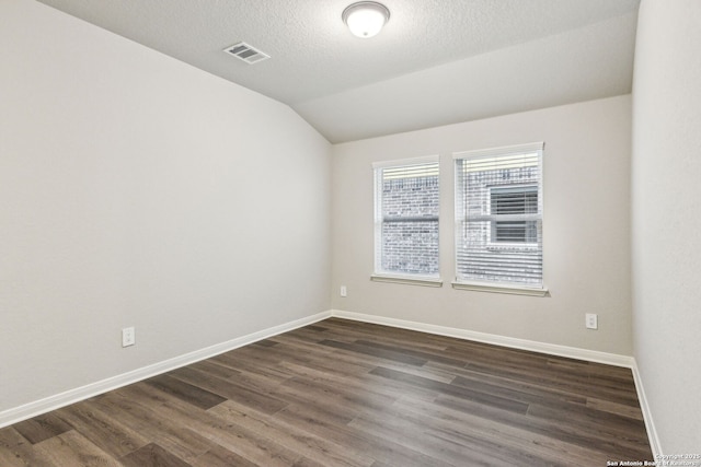 spare room featuring vaulted ceiling, dark hardwood / wood-style floors, and a textured ceiling