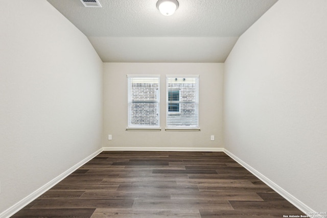 empty room featuring lofted ceiling, dark hardwood / wood-style flooring, and a textured ceiling