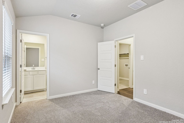 unfurnished bedroom featuring a spacious closet, vaulted ceiling, light colored carpet, and ensuite bathroom