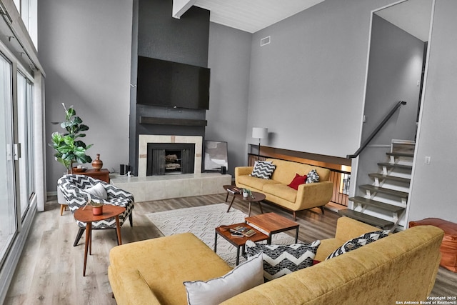 living room featuring a tiled fireplace, light hardwood / wood-style floors, and a high ceiling