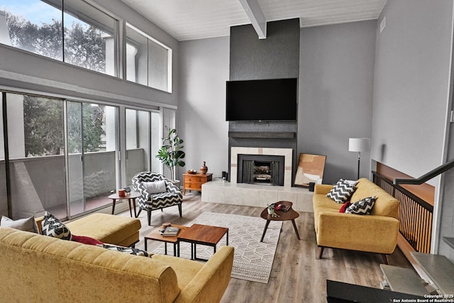 living room featuring beam ceiling, a high ceiling, wood ceiling, a fireplace, and light hardwood / wood-style floors