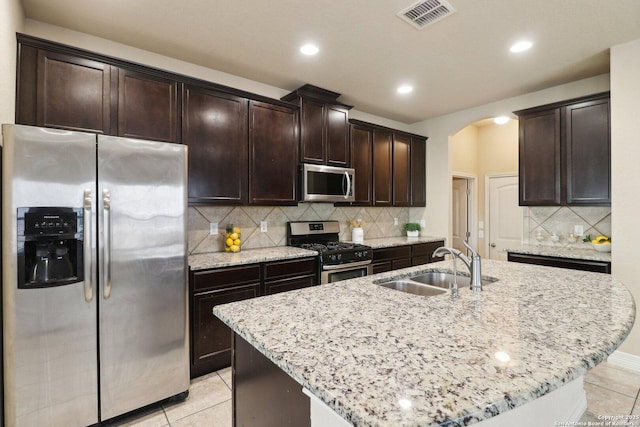 kitchen featuring light tile patterned floors, decorative backsplash, sink, an island with sink, and stainless steel appliances