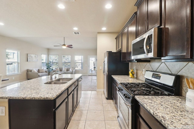 kitchen with an island with sink, light stone countertops, sink, backsplash, and stainless steel appliances