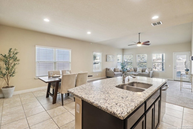 kitchen with light tile patterned flooring, sink, light stone countertops, and an island with sink