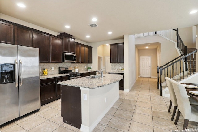 kitchen with appliances with stainless steel finishes, sink, light tile patterned floors, light stone counters, and a center island with sink