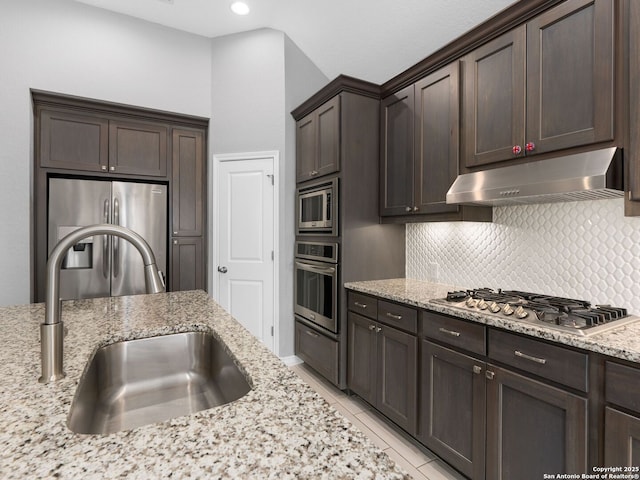 kitchen featuring light stone countertops, sink, dark brown cabinetry, backsplash, and stainless steel appliances