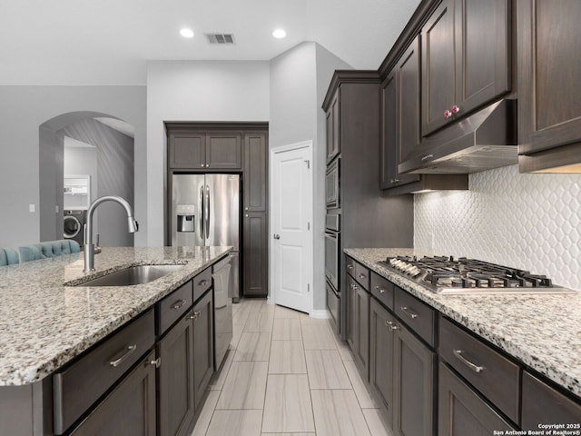 kitchen featuring appliances with stainless steel finishes, washer / clothes dryer, decorative backsplash, sink, and light stone counters