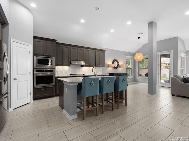 kitchen with appliances with stainless steel finishes, a kitchen island with sink, pendant lighting, a breakfast bar, and vaulted ceiling