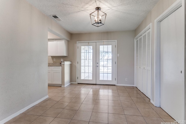 entryway with a textured ceiling, light tile patterned floors, a notable chandelier, and french doors