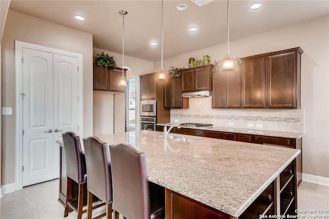 kitchen with appliances with stainless steel finishes, decorative light fixtures, tasteful backsplash, an island with sink, and sink