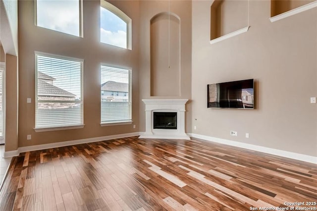 unfurnished living room with a towering ceiling, a healthy amount of sunlight, and hardwood / wood-style floors