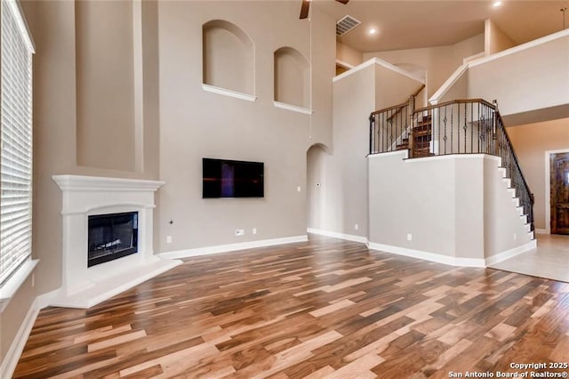 unfurnished living room with hardwood / wood-style floors, a high ceiling, and ceiling fan