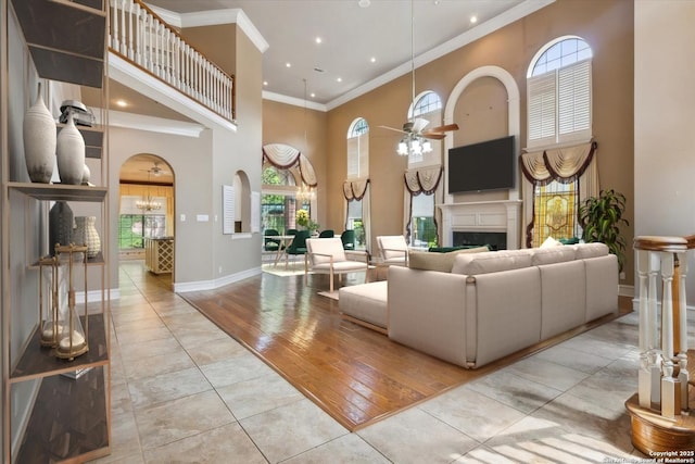 living room with ceiling fan with notable chandelier, a high ceiling, light tile patterned floors, and ornamental molding