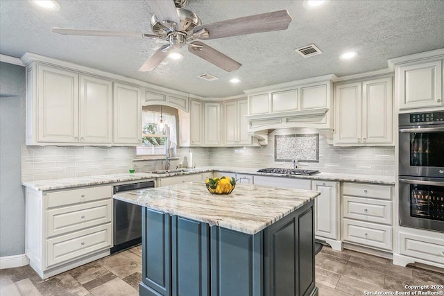 kitchen with light stone countertops, a textured ceiling, appliances with stainless steel finishes, a kitchen island, and sink