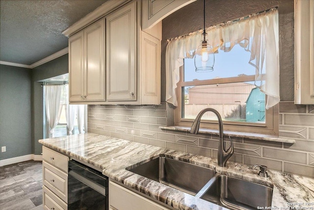 kitchen featuring black dishwasher, sink, backsplash, hanging light fixtures, and cream cabinets