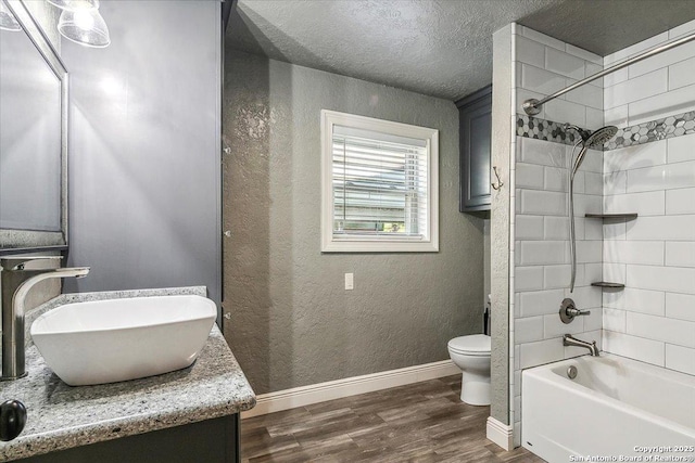 full bathroom with toilet, a textured ceiling, tiled shower / bath combo, hardwood / wood-style flooring, and vanity