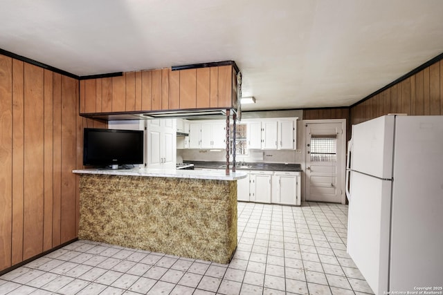 kitchen featuring white cabinetry, white refrigerator, kitchen peninsula, wood walls, and crown molding