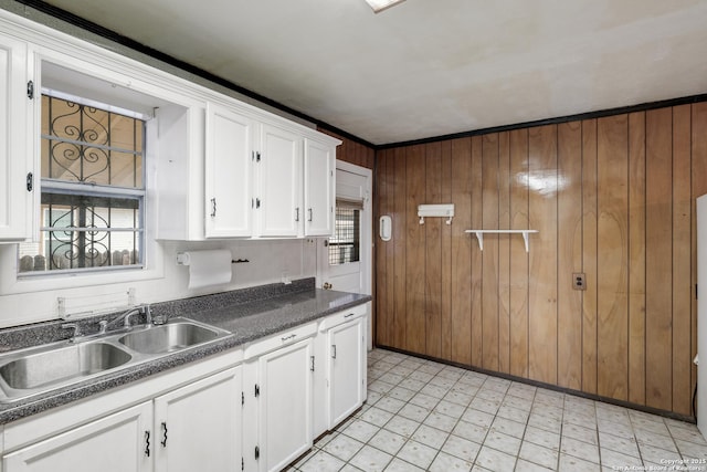 kitchen featuring sink, wooden walls, white cabinetry, and ornamental molding