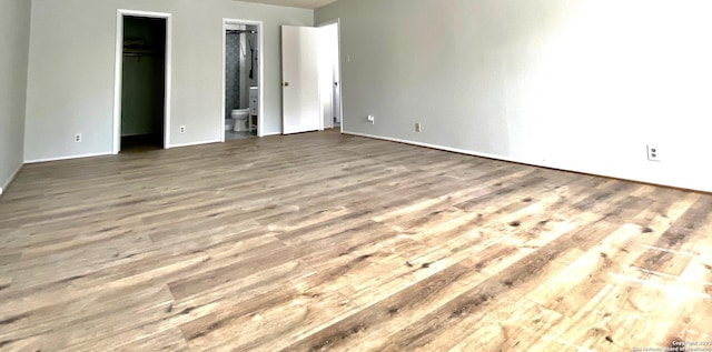 unfurnished bedroom featuring a walk in closet, hardwood / wood-style flooring, and ensuite bath