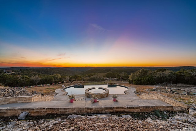 pool at dusk with a patio area and a fire pit