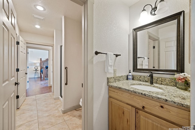 bathroom with a textured ceiling, toilet, tile patterned flooring, and vanity