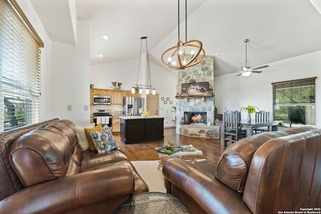 living room with ceiling fan with notable chandelier, hardwood / wood-style floors, high vaulted ceiling, and a stone fireplace