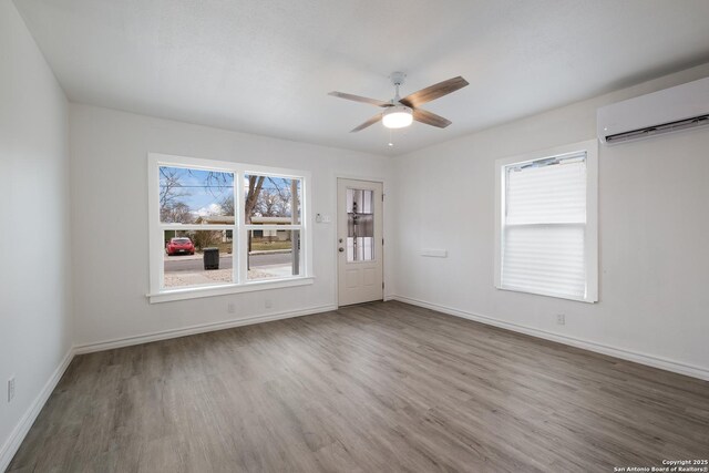 unfurnished room featuring hardwood / wood-style flooring, a wall unit AC, ceiling fan, and a healthy amount of sunlight