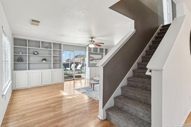 stairs with hardwood / wood-style flooring, a textured ceiling, and ceiling fan