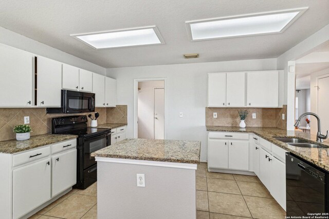 kitchen featuring black appliances, light stone countertops, white cabinetry, sink, and a kitchen island