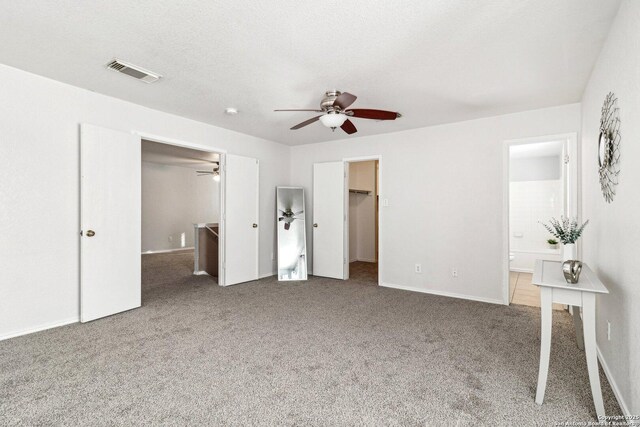 unfurnished bedroom featuring ceiling fan, carpet flooring, ensuite bath, a spacious closet, and a closet