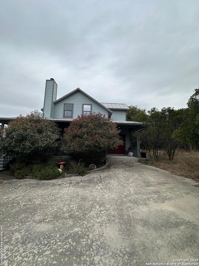 view of front of property featuring a standing seam roof, metal roof, driveway, and a chimney