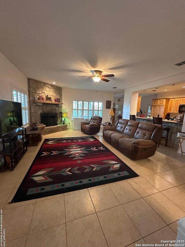 living area with light tile patterned floors, a fireplace, visible vents, and ceiling fan