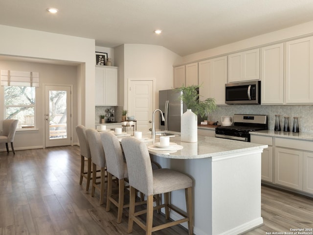 kitchen featuring an island with sink, light hardwood / wood-style floors, decorative backsplash, a breakfast bar, and stainless steel appliances