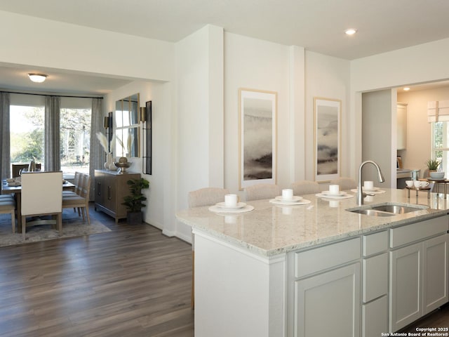 kitchen with light stone countertops, white cabinets, dark hardwood / wood-style flooring, sink, and a center island with sink