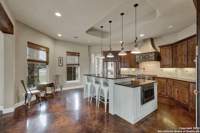 kitchen featuring hanging light fixtures, a raised ceiling, custom range hood, a kitchen island, and stainless steel appliances