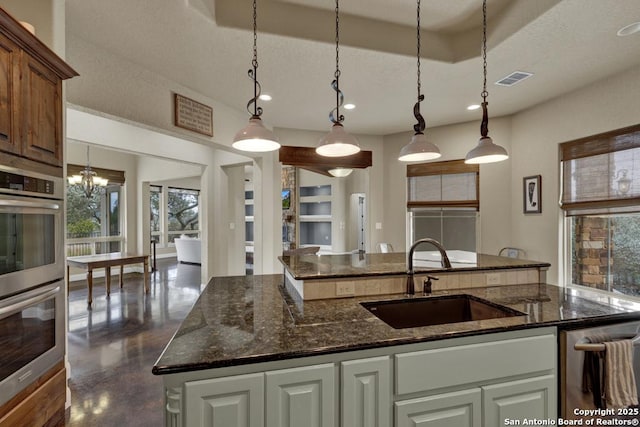 kitchen featuring a center island with sink, sink, hanging light fixtures, and white cabinets