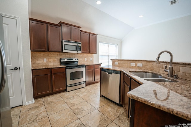 kitchen featuring light stone countertops, vaulted ceiling, sink, dark brown cabinetry, and stainless steel appliances