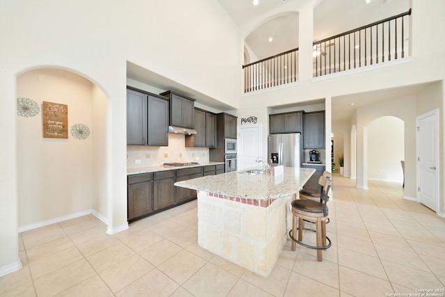 kitchen with a high ceiling, light tile patterned floors, stainless steel appliances, and an island with sink