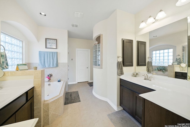 bathroom with tile patterned floors, a relaxing tiled tub, and vanity