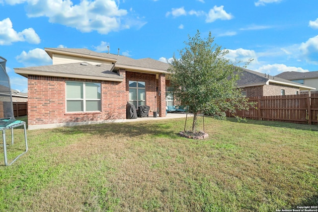 rear view of property featuring a patio area, a yard, and a trampoline