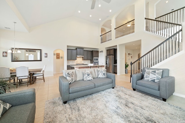 living room featuring high vaulted ceiling, light tile patterned floors, and ceiling fan with notable chandelier